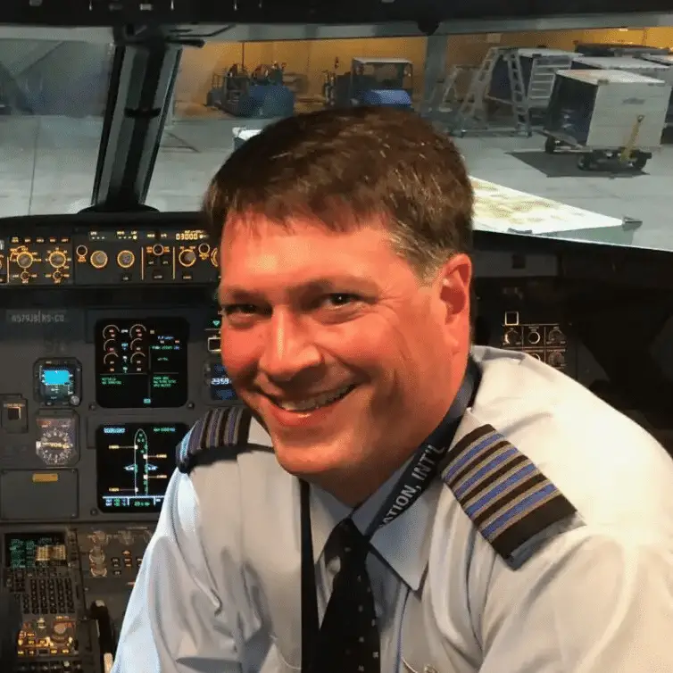 smiling airline captain in uniform seated in illuminated commercial aircraft cockpit with flight instruments.